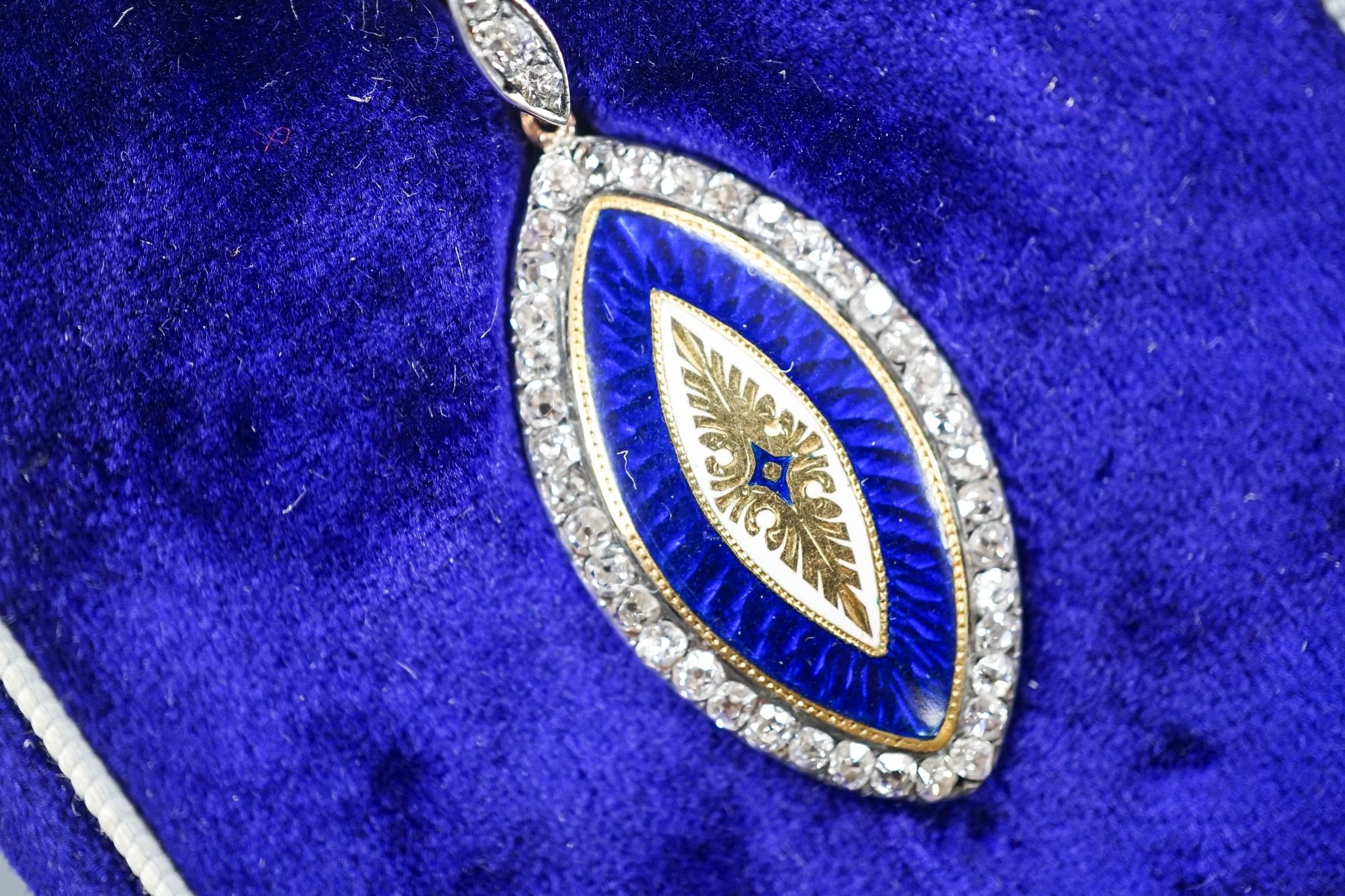 An early 20th century yellow metal, two colour enamel and diamond set navette shaped pendant, 32mm, on a yellow metal chain, 47cm, gross weight 6.9 grams.